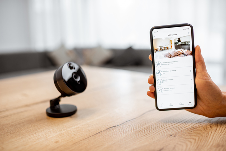 Close-up on a smart phone with launched security application and wireless camera at the table.