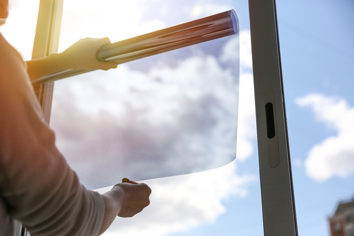 tinted glass in the house. window dimming by dark film. hands apply tint film to the window. tint film on sky background. sky view through tinted glass