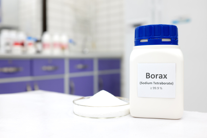 Selective focus of a bottle of borax chemical compound or sodium tetraborate beside a petri dish with solid powder substance. White Chemistry laboratory background with copy space.