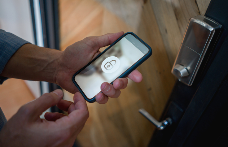 Close-up on a man opening the door of his house using a home automation system on his cell phone.