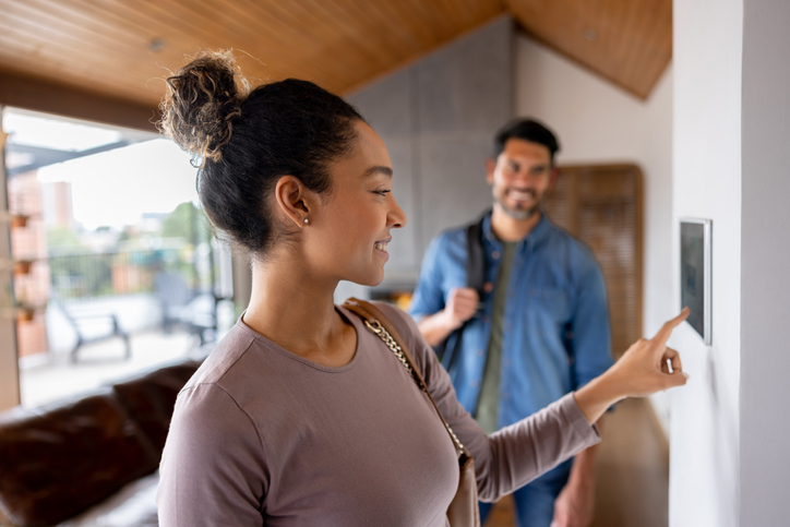 A happy couple leaving their house and setting the alarm using a home automated system