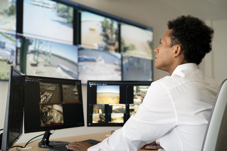 Young adult male security worker watching video wall while sitting at desk