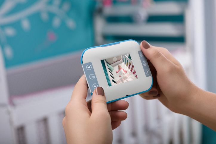 Caucasian female hands holding a baby monitor, with a crib background