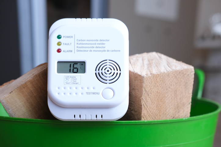 Detail shot of a carbon monoxide alarm or CO warning device in a basket of firewood in an apartment in front of a fireplace.