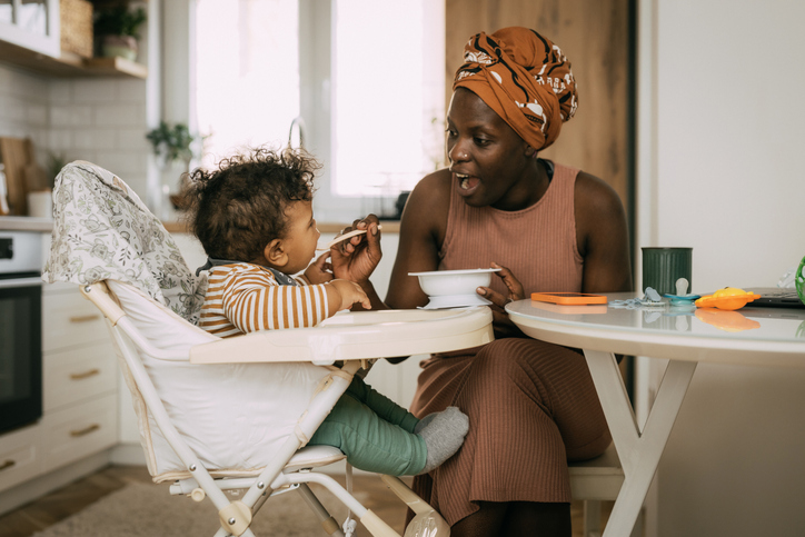 Young mother feeding her baby boy in the living room at home