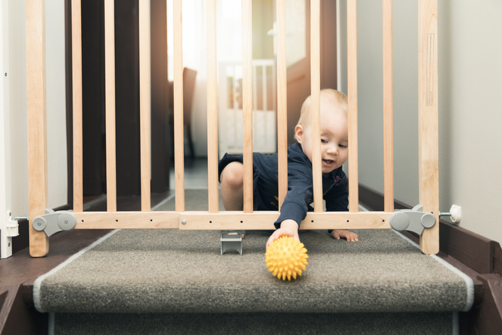 child playing behind safety gates in front of stairs at home