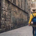 A shot of a female tourist in a yellow jacket, pulling a rolling suit case down a brick street