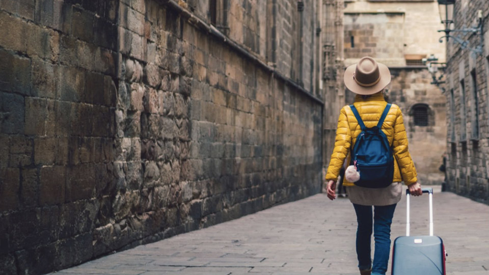 A shot of a female tourist in a yellow jacket, pulling a rolling suit case down a brick street