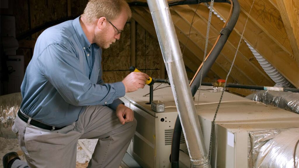 HVAC repair technician servicing a furnace in the attic.