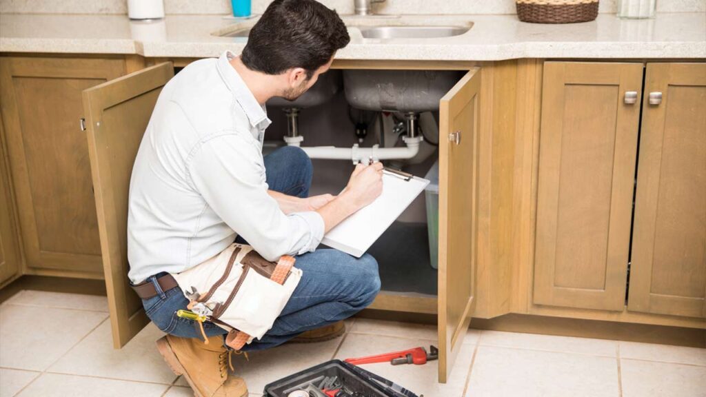 A contract plumber working on pipe inspection underneath kitchen sink